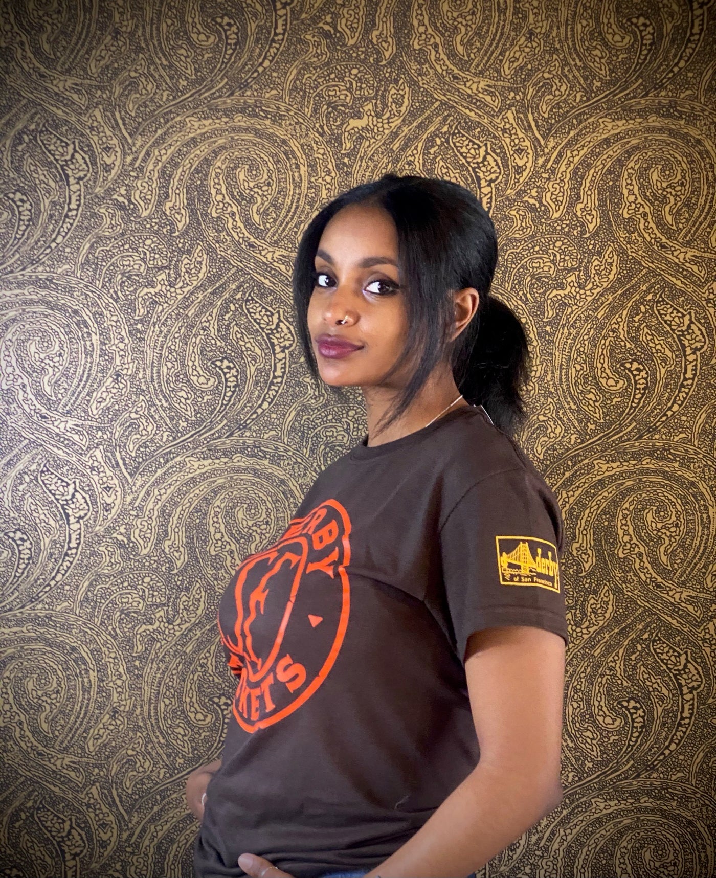 woman in Derby t-shirt standing in front of gold paisley wall