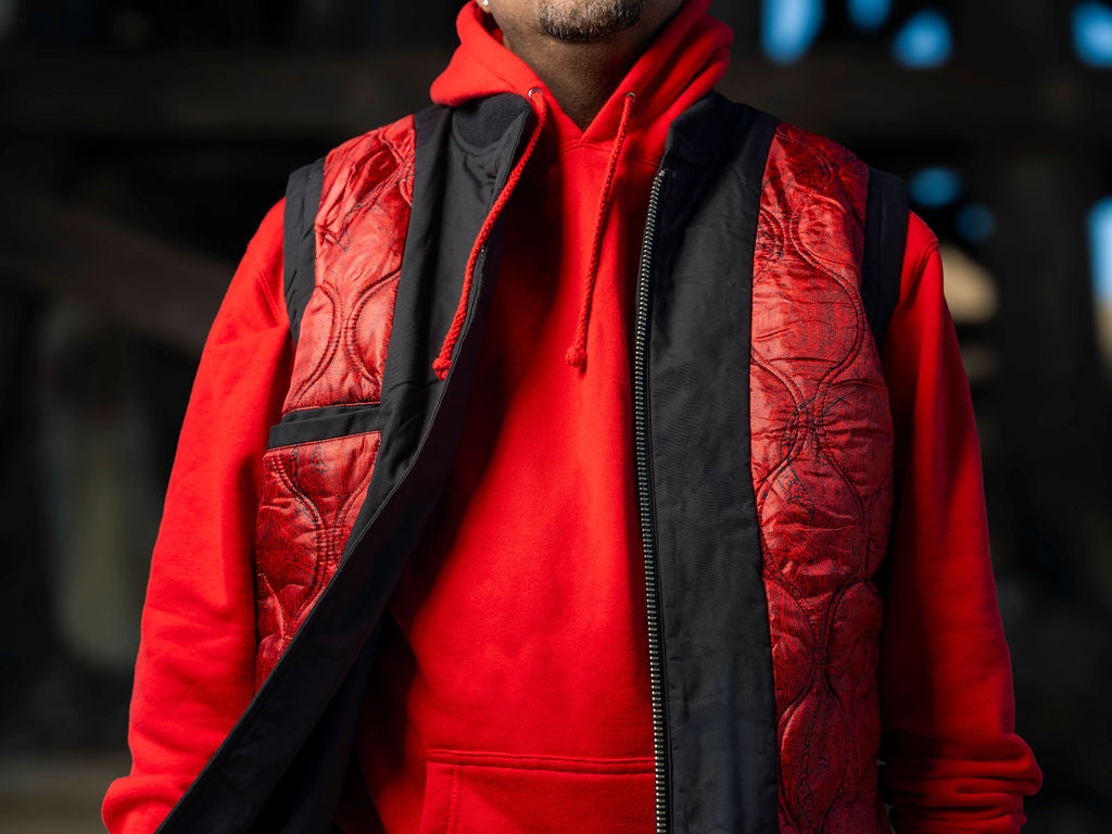 Person wearing a red hoodie with a black quilted vest over it, against a dark background.
