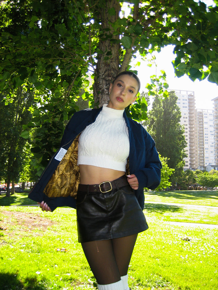 Person in a park wearing a white top, black skirt, and dark jacket.