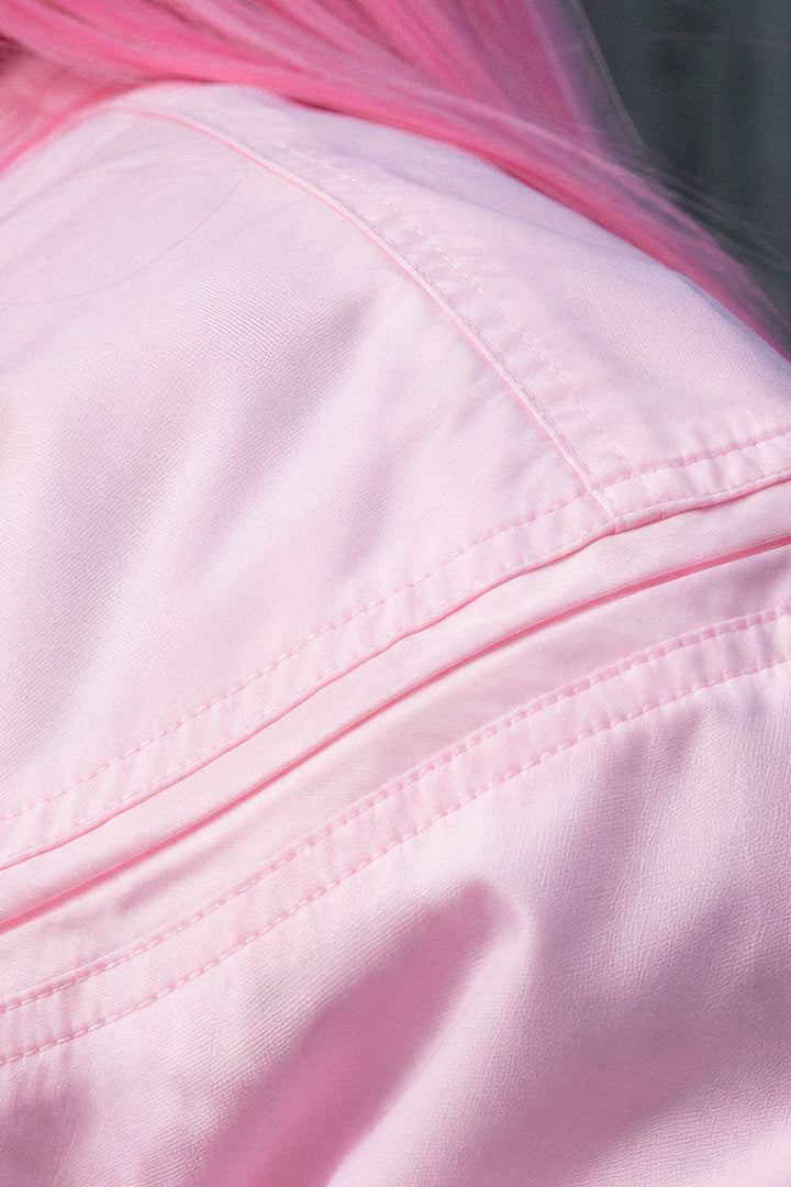 Close-up of a light pink fabric garment with visible stitching and a bright pink hair or fabric accent at the top edge.