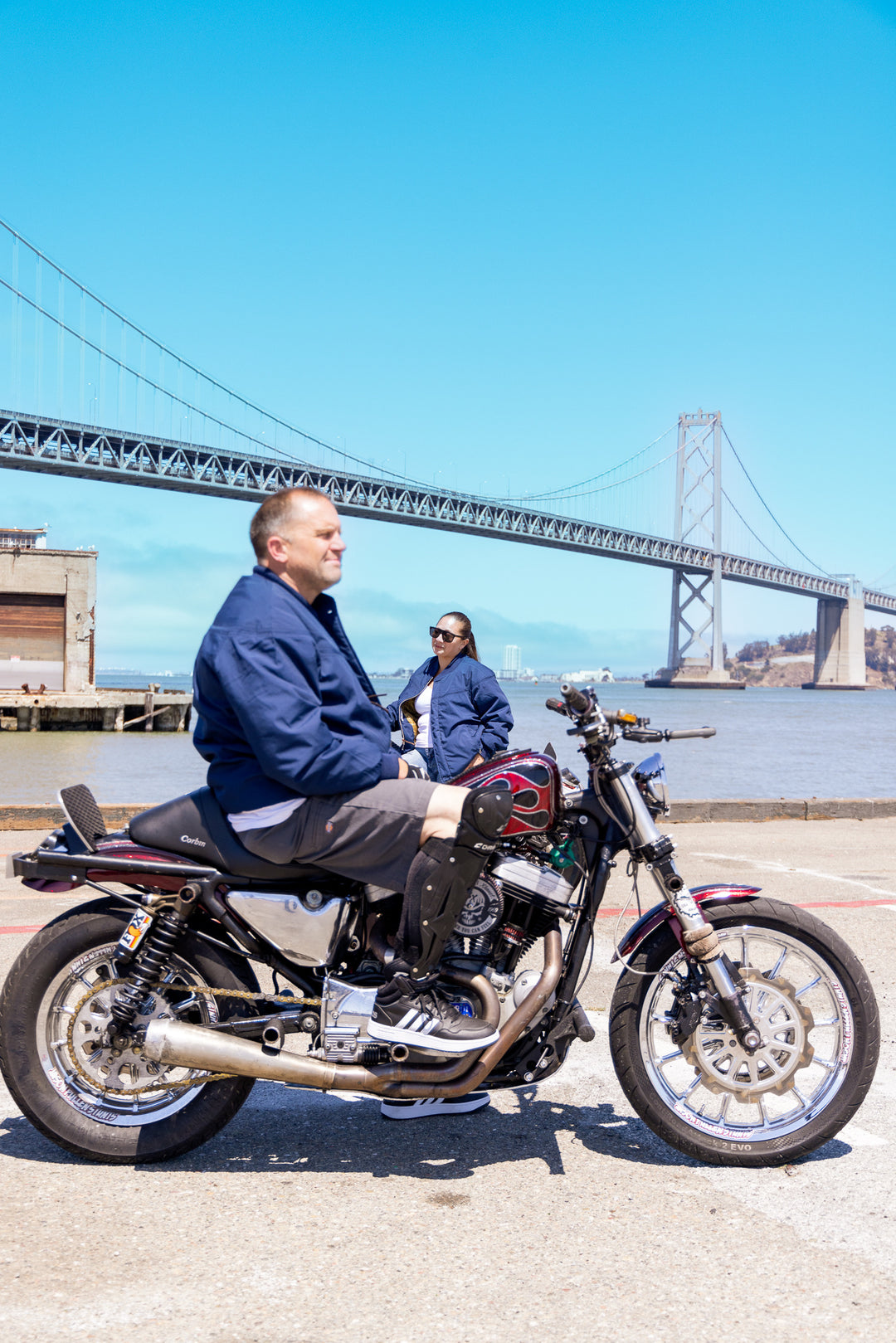 Person sitting on a motorcycle with a bridge and water in the background