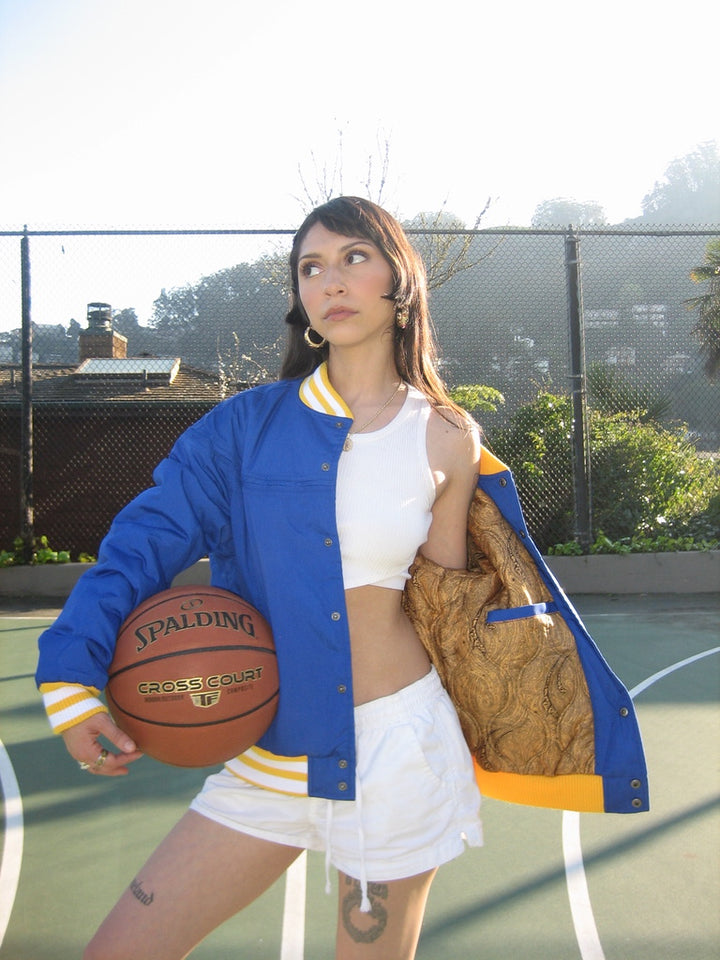 Person holding a basketball on a court wearing a blue and gold jacket.