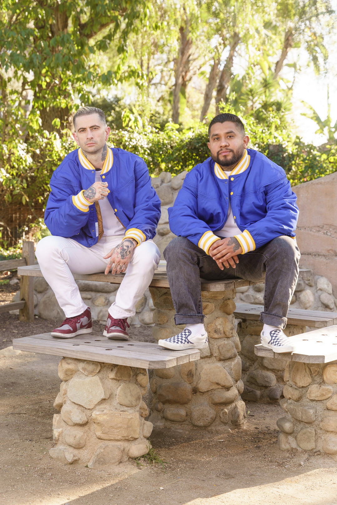 Two men in blue jackets sitting on stone benches in a park.