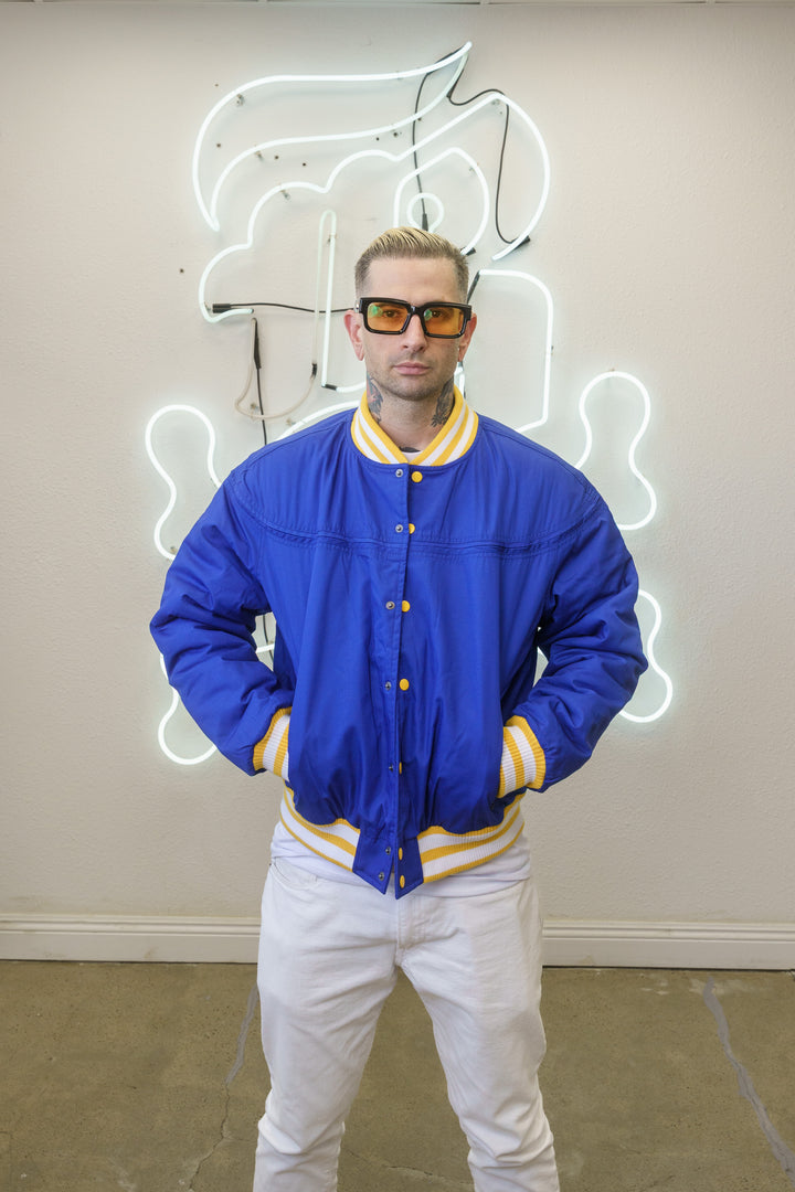 Man wearing a blue jacket with yellow accents standing in front of a neon sign.