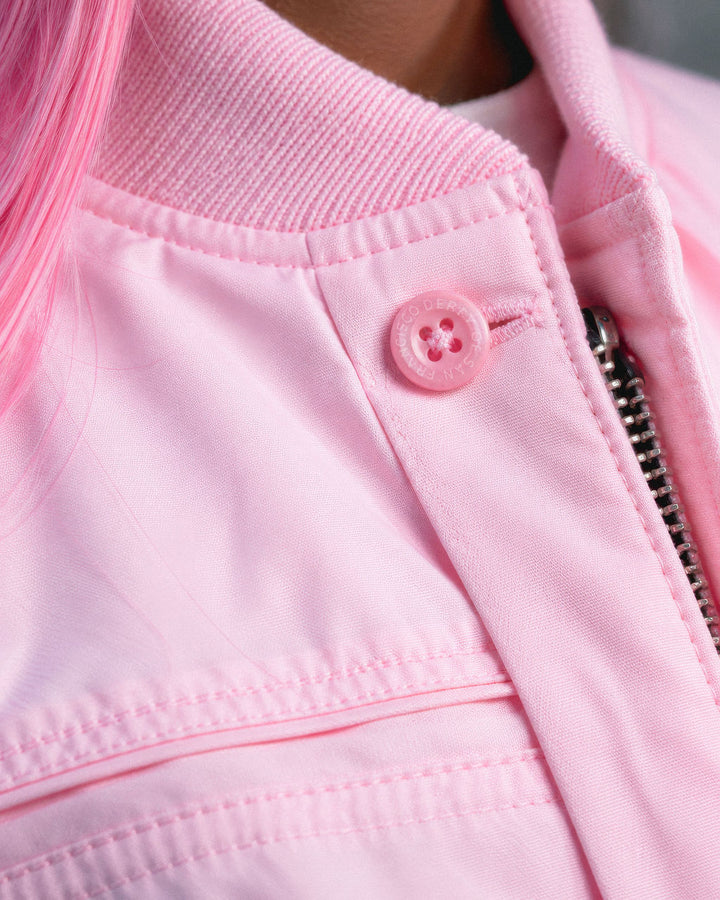 Close-up of a light pink jacket with a matching pink button, zipper, and ribbed collar, showing part of a person&