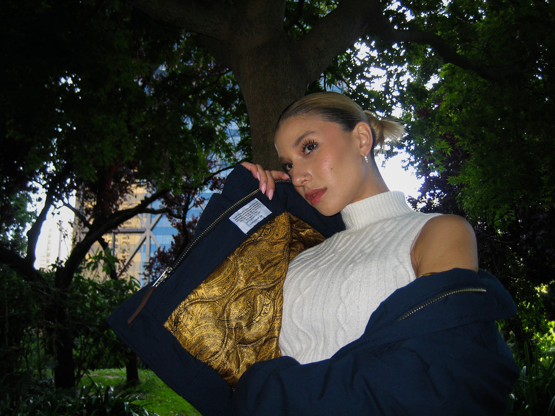Woman holding a dark blue garment with gold patterns in an outdoor setting