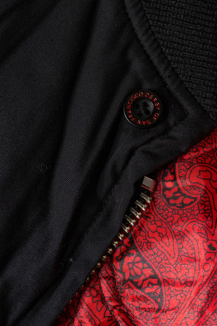 Close-up of a black garment with a red paisley pattern inside, featuring a button and zipper.
