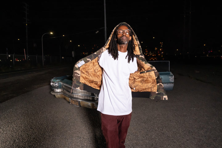 Person holding a camouflage-patterned bag in front of a vintage car at night.