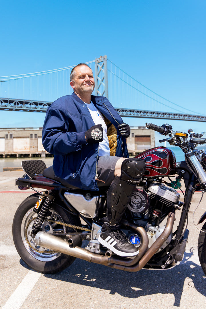 Man sitting on a motorcycle with a bridge in the background
