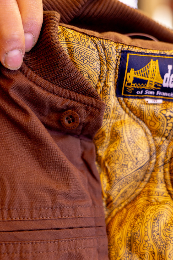 Close-up of brown pants with a patterned label featuring a bridge design.