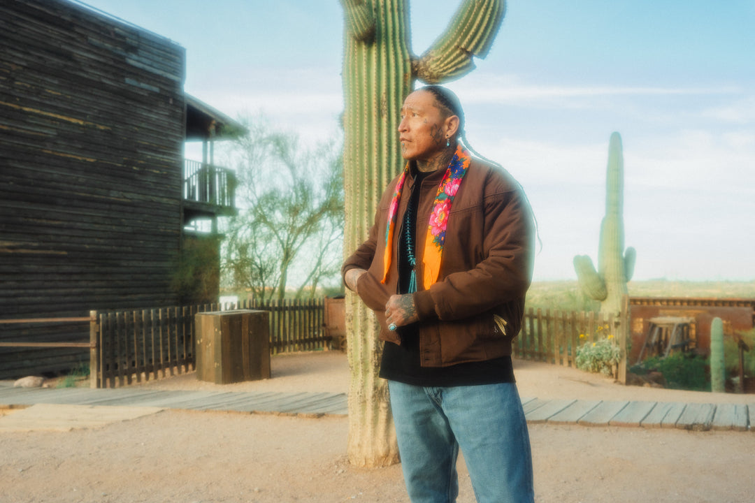 Person standing in front of a cactus with a building and desert landscape in the background