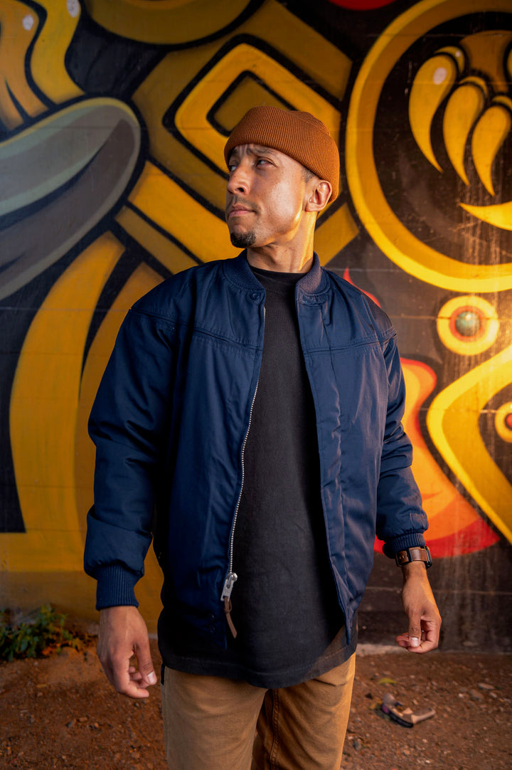 A person wearing a navy blue derby jacket with a gold paisley pattern, sitting in front of a fire engine.