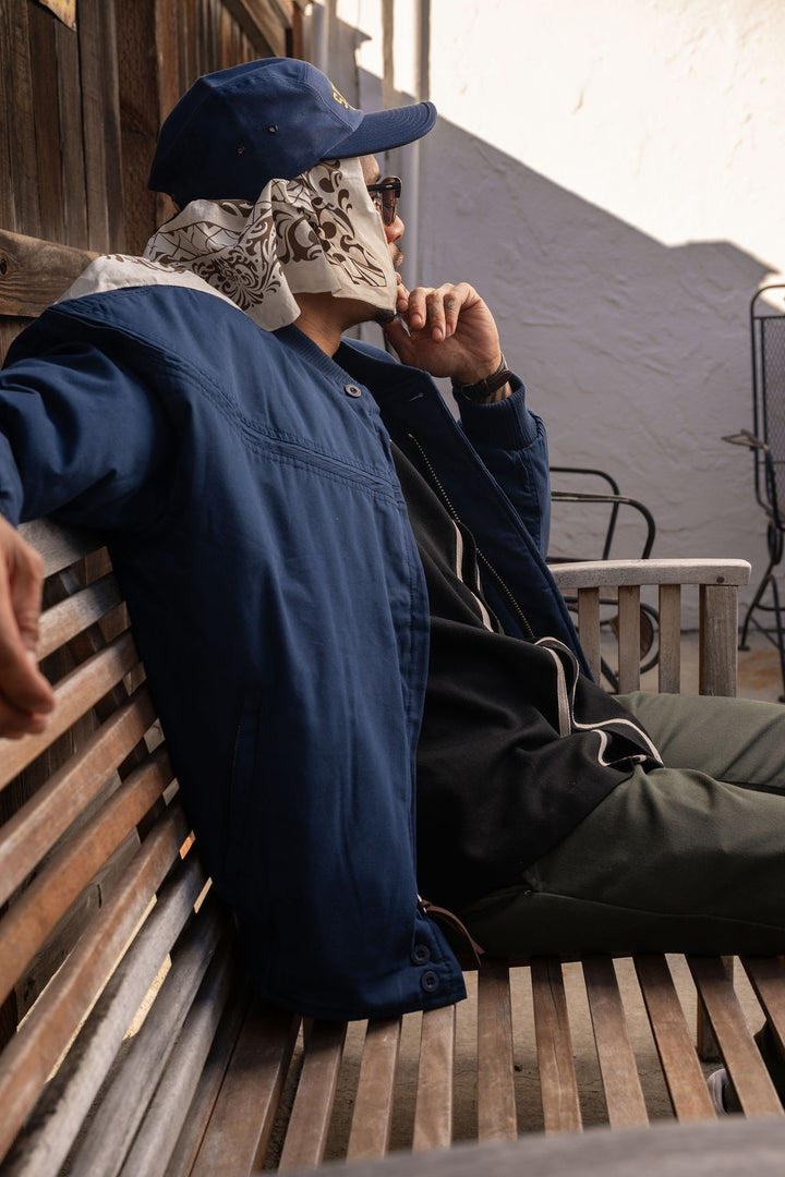 Person wearing a blue jacket and cap sitting on a wooden bench.