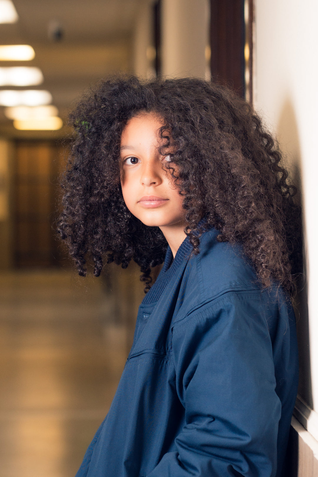 Person with curly hair wearing a blue jacket in an indoor setting