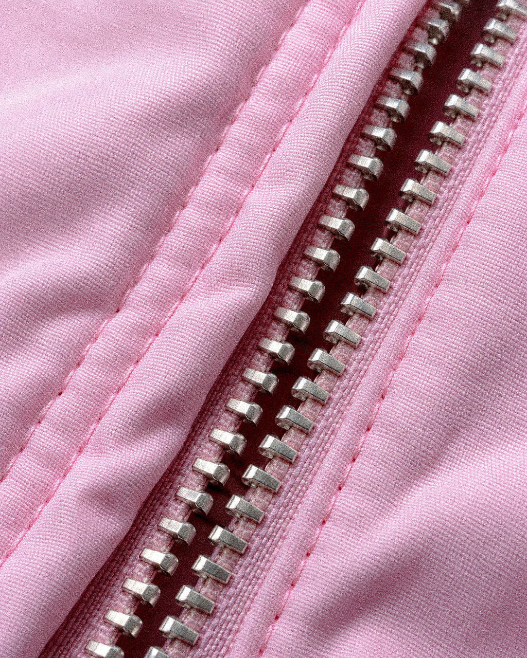 Close-up of a light pink fabric jacket with a silver metal zipper running vertically through the center.